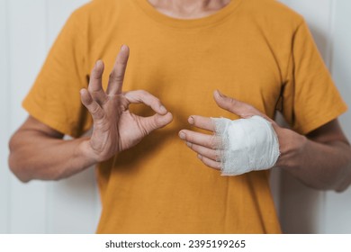 An individual wearing a yellow shirt with their left hand wrapped in a white bandage, possibly indicating an injury. - Shutterstock ID 2395199265