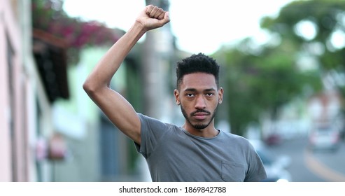 Individual Young Black Man Raising Fist In Air Staring Camera In Protest. Rebel African Mixed Race Ethnicity