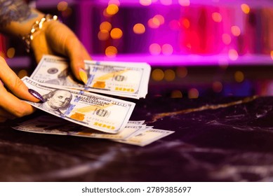 Individuals exchanging hundred dollar notes against neonlit festive setting. Multiple hands organizing hundred dollar bills on plush velvet with lively neon backdrop and celebratory atmosphere