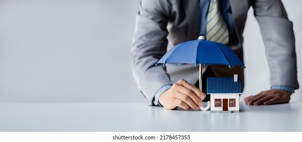 Individuals holding small umbrellas and model homes, housing insurance against impending loss and fire, building fire insurance, home and real estate insurance concepts. - Shutterstock ID 2178457353
