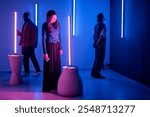 Individuals observing light sculptures in modern art gallery with neon blue and pink lighting creating an immersive, thoughtful environment