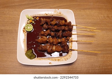 Indonesian Chinese traditional food named "Sate babi manis" i.e. sweet pork satay served on plate with soysauce and a cut of lime and chili sauce, top view 