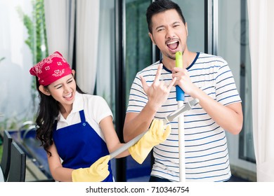 Indonesian Couple Having Fun Cleaning The Home, Woman And Man Playing Air Guitar On Duster And Broom