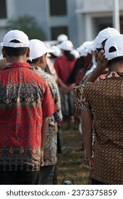 Indonesian elementary school students using batik and white hat on flag raising ceremony in commemmorating Indonesian independence day