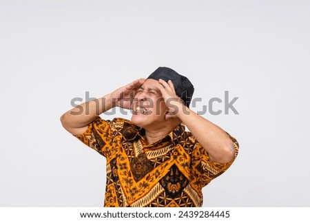 Indonesian man in batik shirt and kopiah expressing frustration, clutching his head looking fed up. isolated on a white background with copy space.