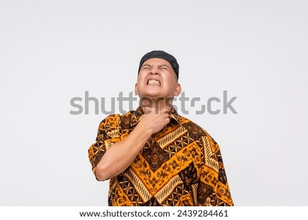 Indonesian man in batik shirt and kopiah appears thirsty and uncomfortable, isolated on a white background.