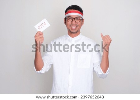 Indonesian man smiling and showing his little finger while holding election vote paper