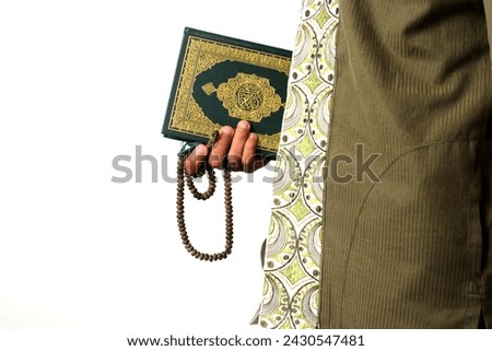 An Indonesian Muslim man holding the Holy Quran and tasbih on a white background prepares to perform Itikaf at a mosque during the last ten days of Ramadan, seeking spiritual reflection and renewal