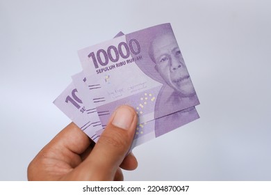 Indonesian Rupiah The Official Currency Of Indonesia. Man's Hand Is Making A Payment. Male Hand Showing Indonesian Rupiah Note. Uang 10000 Rupiah