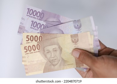 Indonesian Rupiah The Official Currency Of Indonesia. Man's Hand Is Making A Payment. Male Hand Showing Indonesian Rupiah Note. Uang 10000 And 5000 Rupiah