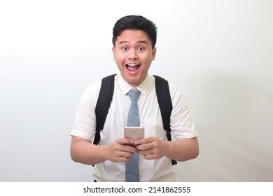 Indonesian Senior High School Student Wearing White Shirt Uniform With Gray Tie Showing Shocked Face Expression While Holding A Mobile Phone. Isolated Image On White Background