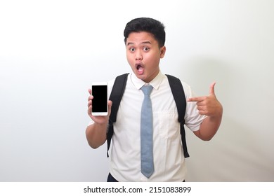 Indonesian Senior High School Student Wearing White Shirt Uniform With Gray Tie Showing And Presenting Blank Screen Mobile Phone While Pointing On His Smartphone. Isolated Image On White Background