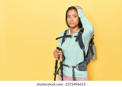 Indonesian woman with hiking gear on yellow being shocked, she has remembered important meeting.