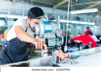 Indonesian worker using a cutter - a large machine for cutting fabrics - in a asian textile factory, he wears a chain glove