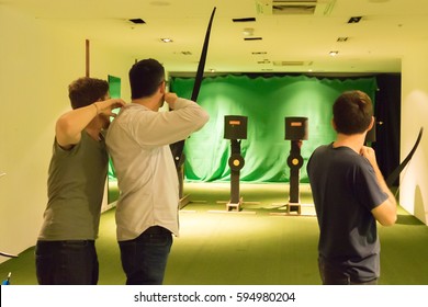 Indoor Archery Range, Instructor Guiding A Man Aiming Drawn Bow In Front Of Targets