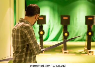 Indoor Archery Range, Single Man Notching An Arrow Onto A Bow Facing Towards Targets