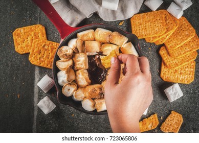 Indoor Sâ??mores, Baked Sâ??mores Dip In A Cast Iron Skillet Pan With Graham Crackers. Girls Hand In Picture, Tasting Smores, Dark Grey Table, Top View Copy Space