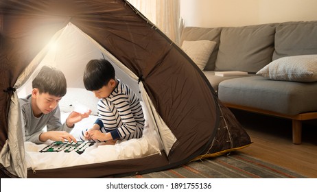 Indoor camping tent - Stay at home activity for family during Covid 19 pandemic lockdown concept. Young asian brothers kids playing games together in a teepee in living room. Happy, siblings, april 10