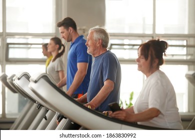 Indoor Cardio Workout. Elderly Man And Woman Walking On Treadmill, Focus On Man. Sport For Seniors.