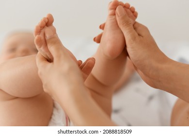 Indoor closeup shot of mother hands doing gymnastics her baby infant, unknown faceless woman doing feet massage to toddler little child.
