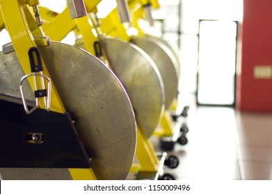 Indoor Cycling Spin Bike Wheel Yellow Steel Frame In Row Close Up High Light Window Background