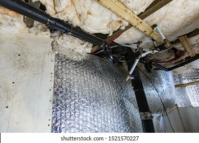 Indoor damp & air quality (IAQ) testing. A low angle view on the walls, joists and structural details inside a basement, details seen beneath the plasterboard, with insulation and plumbing.