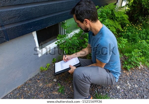 Indoor damp & air quality (IAQ) testing. A\
close up view on environmental home quality inspector at work,\
filling in a form as he inspects the exterior of a cellar window,\
with room for copy.