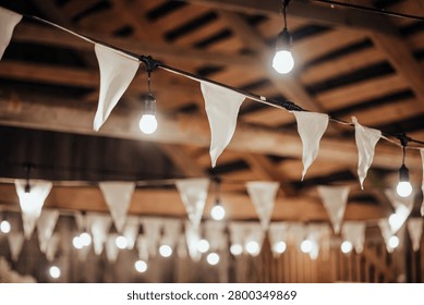 Indoor decorative string lights and white fabric bunting hang beneath a wooden ceiling, creating a warm festive atmosphere with soft bokeh