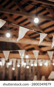 Indoor decorative string lights and white fabric bunting hang beneath a wooden ceiling, creating a warm festive atmosphere with soft bokeh