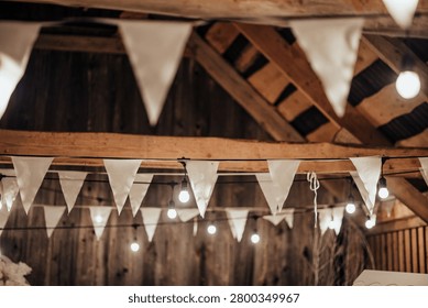 Indoor decorative string lights and white fabric bunting hang beneath a wooden ceiling, creating a warm festive atmosphere with soft bokeh