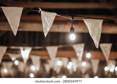 Indoor decorative string lights and white fabric bunting hang beneath a wooden ceiling, creating a warm festive atmosphere with soft bokeh