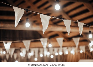 Indoor decorative string lights and white fabric bunting hang beneath a wooden ceiling, creating a warm festive atmosphere with soft bokeh