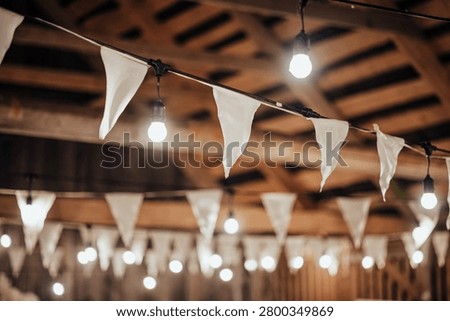 Indoor decorative string lights and white fabric bunting hang beneath a wooden ceiling, creating a warm festive atmosphere with soft bokeh