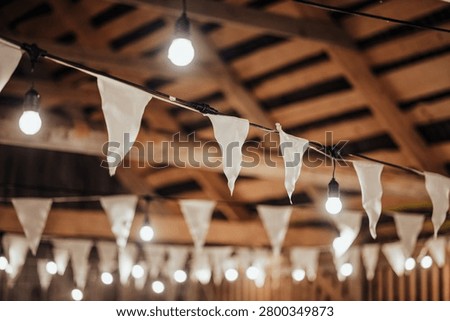Indoor decorative string lights and white fabric bunting hang beneath a wooden ceiling, creating a warm festive atmosphere with soft bokeh