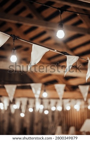 Indoor decorative string lights and white fabric bunting hang beneath a wooden ceiling, creating a warm festive atmosphere with soft bokeh