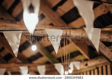 Indoor decorative string lights and white fabric bunting hang beneath a wooden ceiling, creating a warm festive atmosphere with soft bokeh