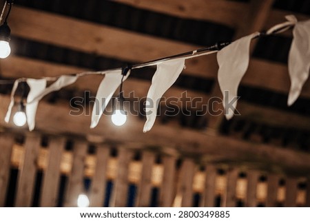 Indoor decorative string lights and white fabric bunting hang beneath a wooden ceiling, creating a warm festive atmosphere with soft bokeh