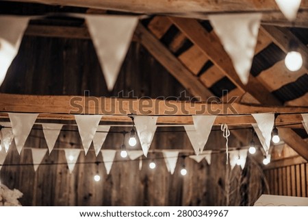 Indoor decorative string lights and white fabric bunting hang beneath a wooden ceiling, creating a warm festive atmosphere with soft bokeh