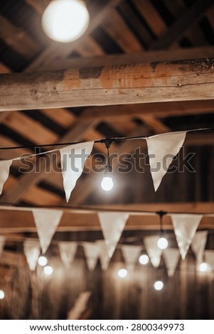 Indoor decorative string lights and white fabric bunting hang beneath a wooden ceiling, creating a warm festive atmosphere with soft bokeh