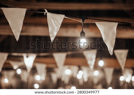 Indoor decorative string lights and white fabric bunting hang beneath a wooden ceiling, creating a warm festive atmosphere with soft bokeh