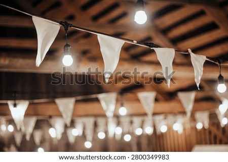 Indoor decorative string lights and white fabric bunting hang beneath a wooden ceiling, creating a warm festive atmosphere with soft bokeh