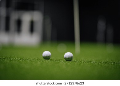 Indoor golf setting with two golf balls resting on synthetic grass, surrounded by putting green and practice area, creating a vibrant sports atmosphere