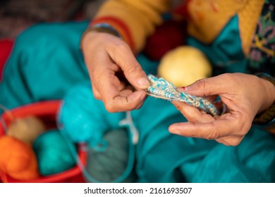 Indoor High Angle Image Of A Happy Indian Woman Sitting On The Bed And Knitting Sweater Woolen In Her Leisure Time At Home. She Is Wearing A Traditional Indian Sari.