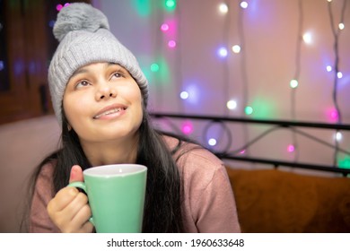 Indoor Image Of An Asian, Indian Beautiful, Happy Young Woman Looking Up And Contemplating While Drinking And Holding A Cup Of Coffee In Winter Season At Home. She Is Wearing Warm Clothes.