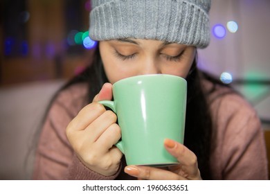 Indoor Image Of An Asian, Indian Beautiful, Serene Young Woman Drinking Coffee Winter Season At Home. She Is Wearing Warm Clothes, Sweater And A Woolen Cap.