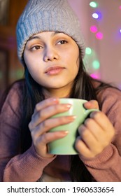 Indoor Image Of An Asian, Indian Beautiful, Serene Young Woman Looking Away And Contemplating While Drinking And Holding A Cup Of Coffee In Winter Season At Home. She Is Wearing Warm Clothes Sweater.