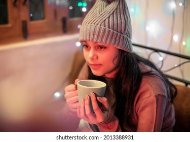 Indoor Image Of An Asian, Indian Beautiful, Serene Young Woman Looking Away And Contemplating While Drinking And Holding A Cup Of Coffee In Winter Season At Home. She Is Wearing Warm Clothes.