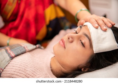 Indoor image of Indian matures mother sponging her ill daughter’s forehead to reduce the temperature down. She is having a high fever and lying in bed at home. She is wearing warm clothes.