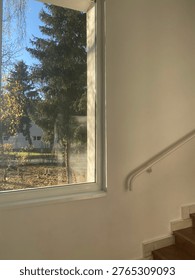 Indoor image with a view through a window to trees in autumn, juxtaposed with a staircase and white wall. Can be used for design inspiration.