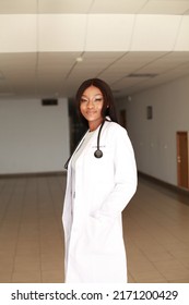 Indoor image of young black African female medical professional wearing white coat uniform and holding stethoscope standing in clinic hall. Concept of underrepresented minorities racial disparities